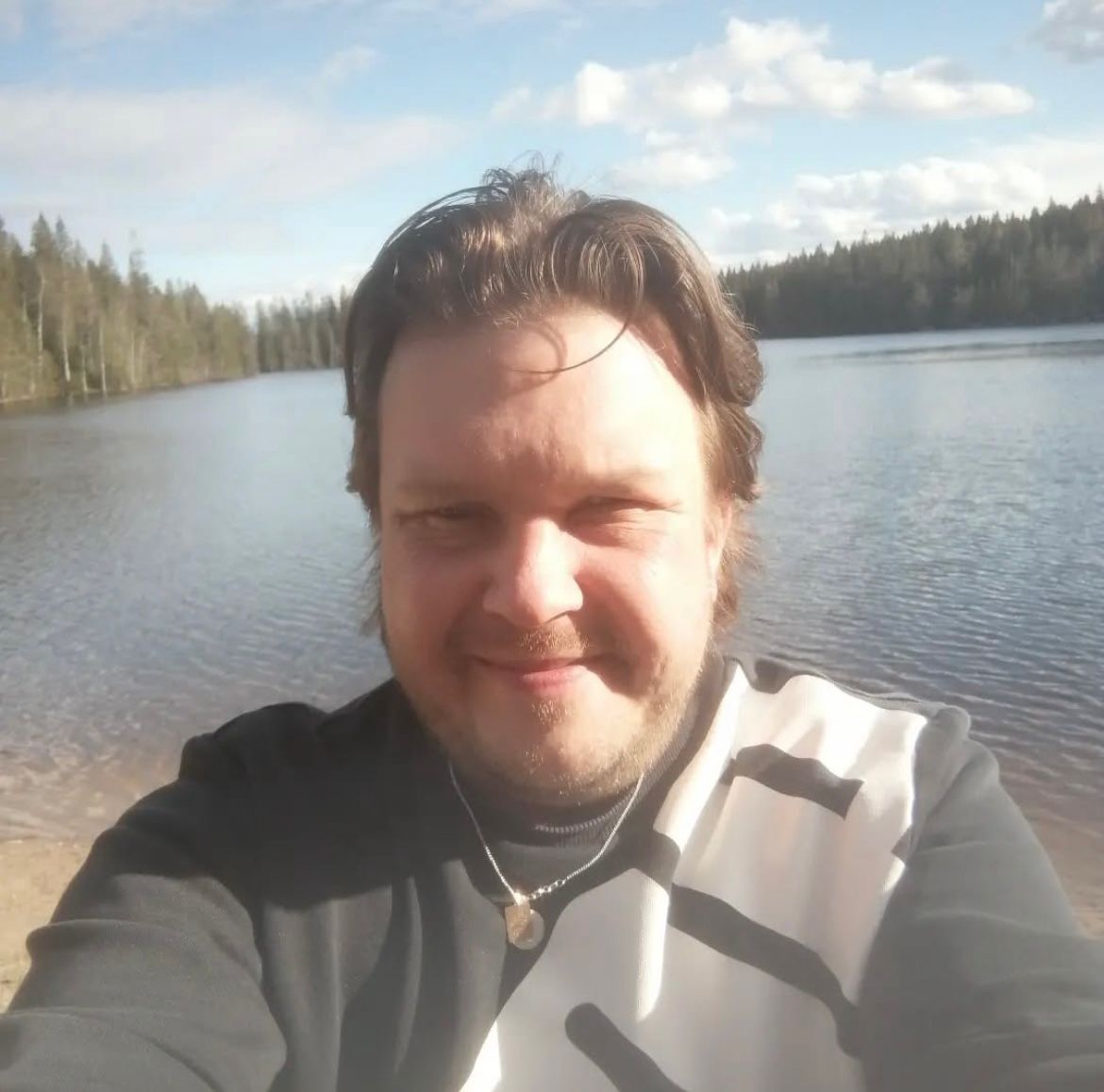 Markus järven rannalla. Järven poukaman takana näkyy metsä.