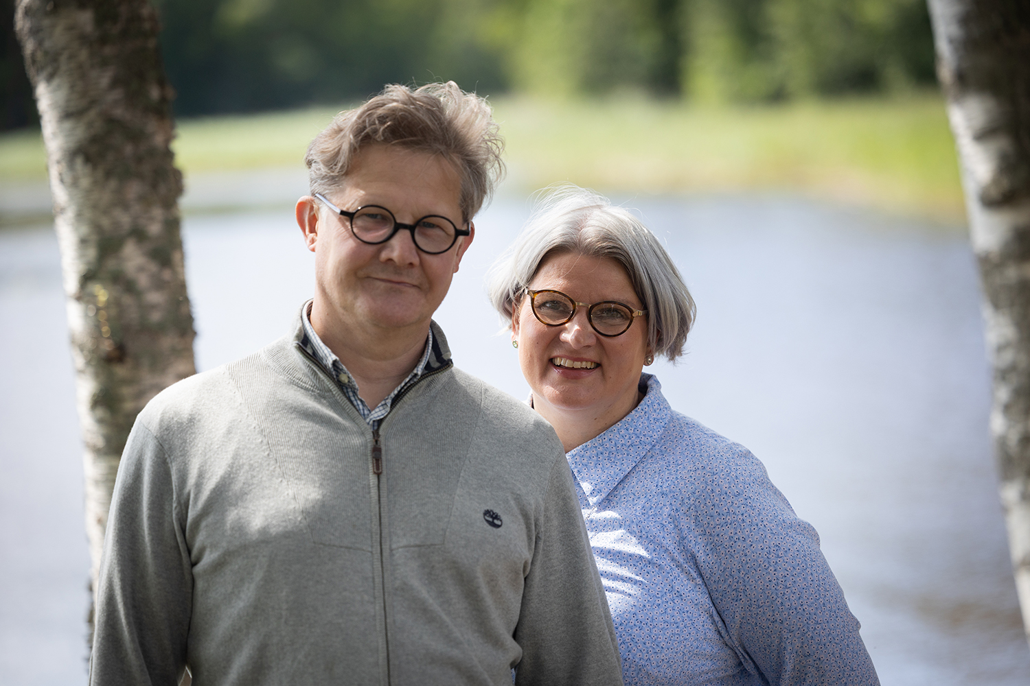 Petri ja Pia-Leena koivun rungon vieressä. Taustalla näkyy järvi.